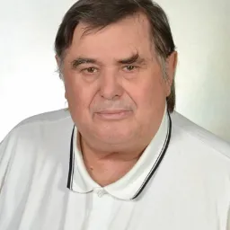 Portret starszego mężczyzny w białej koszulce polo z czarnym paskiem na kołnierzyku, na jasnym, rozmytym tle.