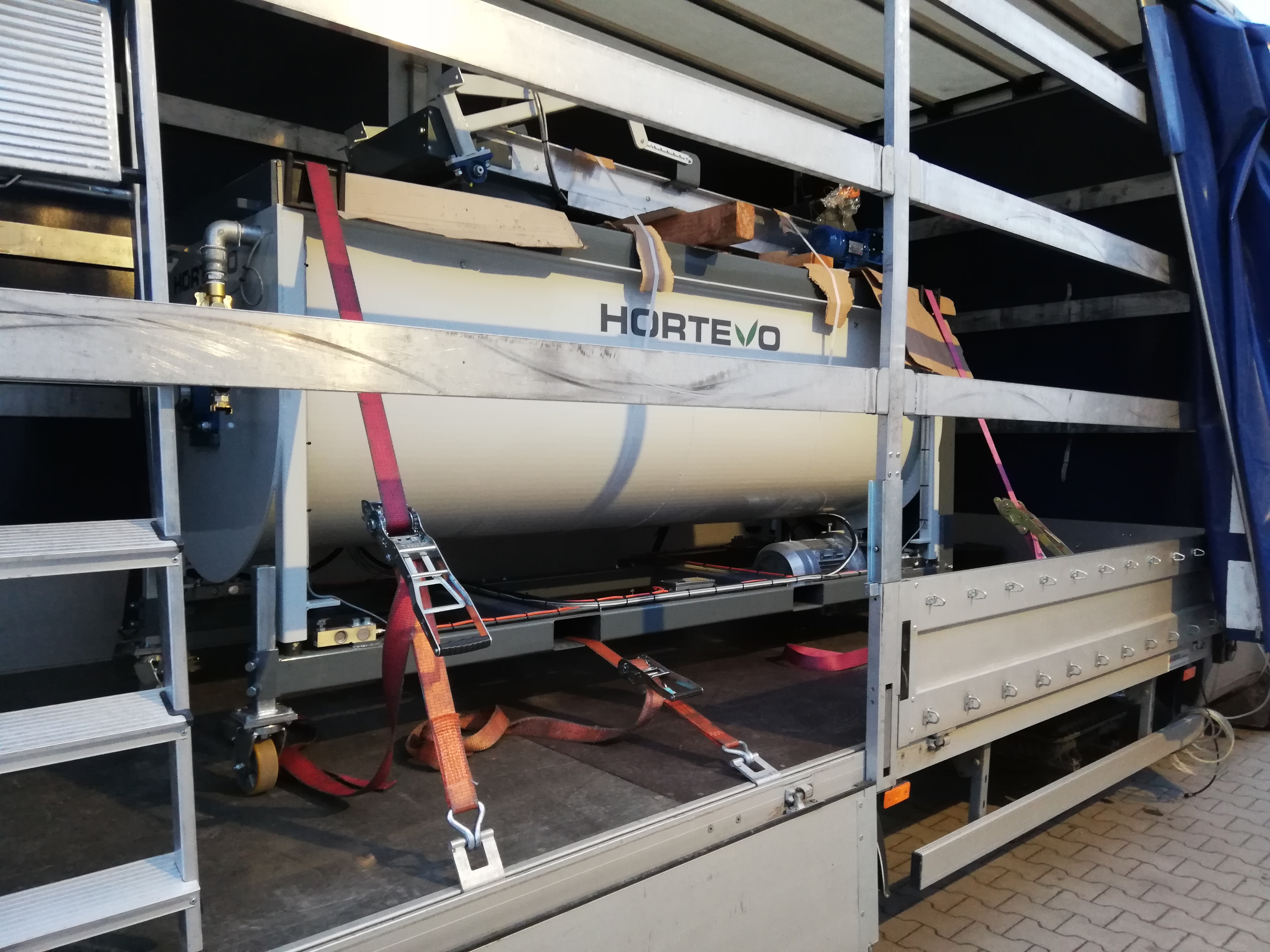 Częściowy widok wnętrza ciężarówki z zabezpieczonym zbiornikiem HORTIVO, przymocowanym czerwonymi pasami transportowymi.