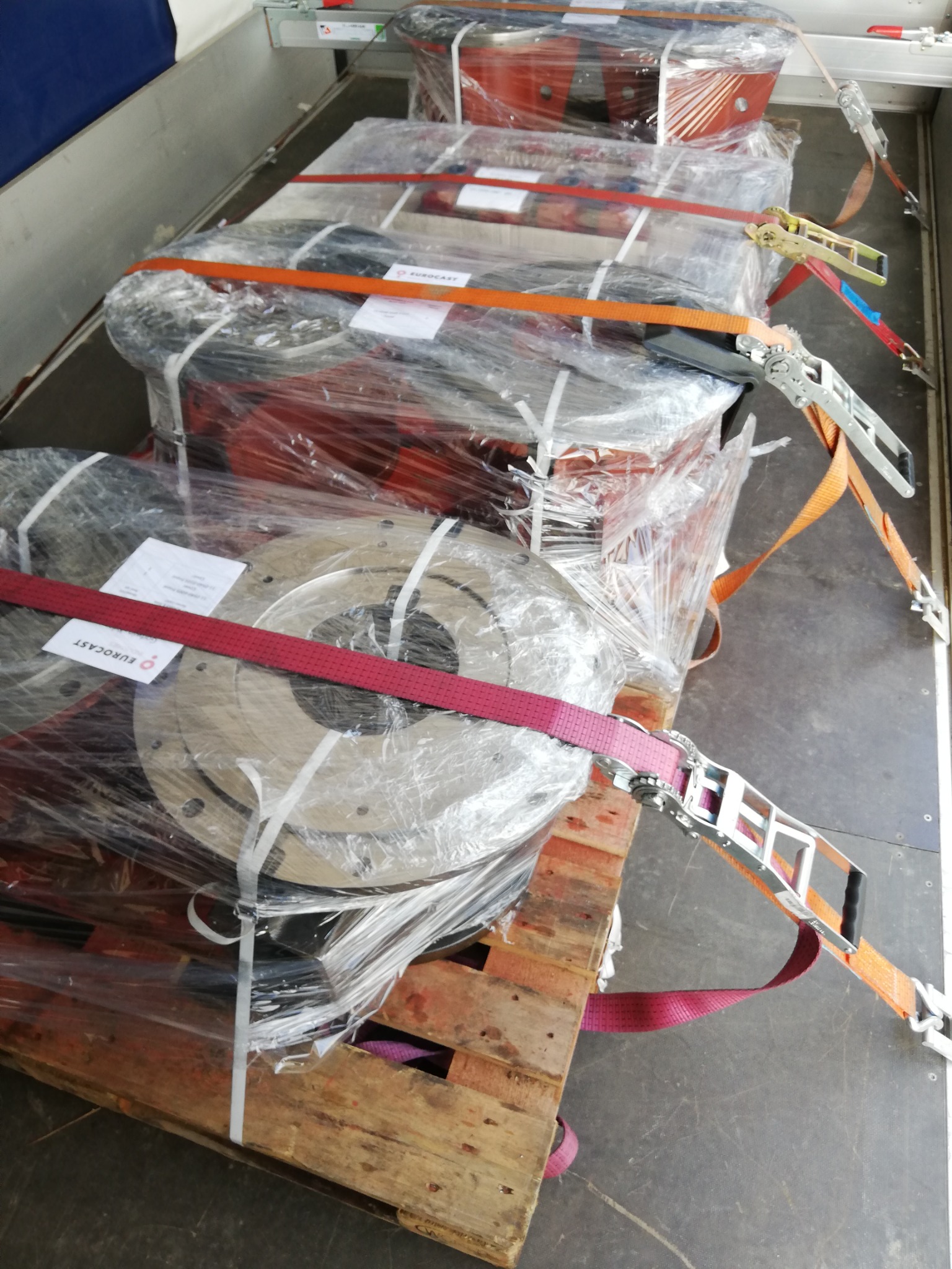 Ładunek zapakowany w folię i zabezpieczony pasami transportowymi wewnątrz pojazdu dostawczego, widoczne palety drewniane.