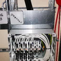 Rozdzielnia antenowa w metalowej obudowie z licznymi przewodami, zamontowana na szynie. Widoczne napisy 'Domofon' na obudowie. Estetyczne ułożenie kabli.