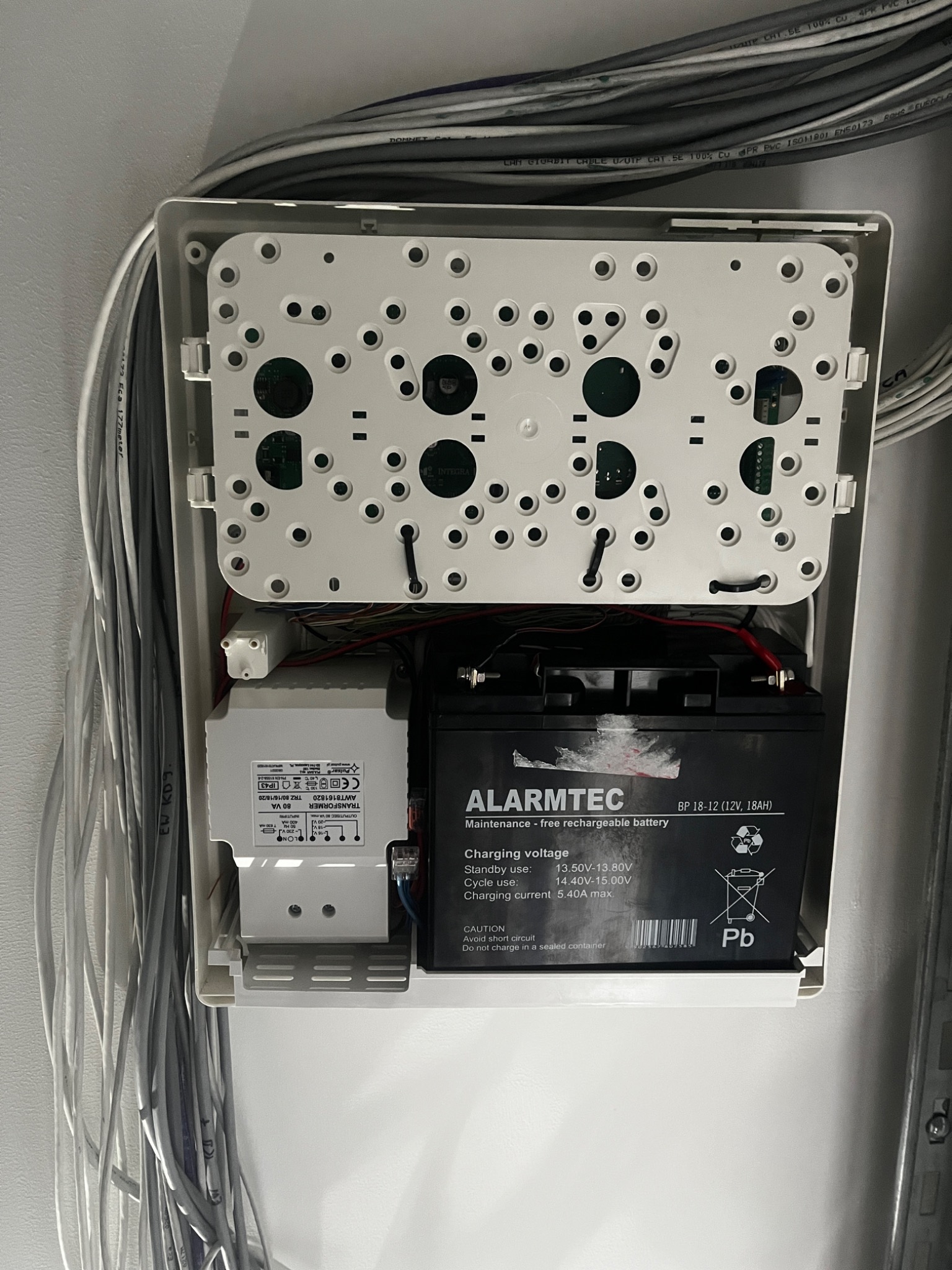 Wnętrze skrzynki alarmowej: akumulator Alarmtec, transformator Pulsar, przewody. Widoczne okablowanie i elementy montażowe.