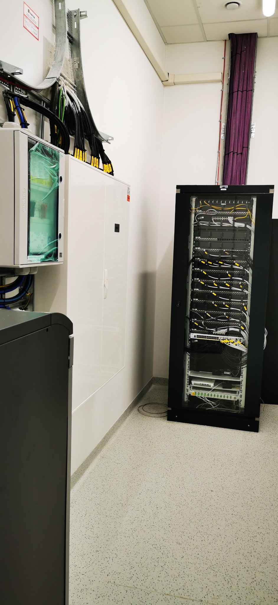 Szafa serwerowa z okablowaniem w pomieszczeniu technicznym w Bydgoszczy. Widoczne kable ułożone w korytach. Białe ściany i szara podłoga.