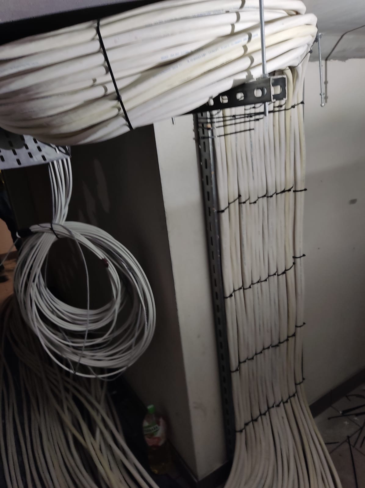 Równolegle ułożone białe kable, spięte czarnymi opaskami, prowadzone w korycie przymocowanym do sufitu. Część kabli zwinięta w spiralę.