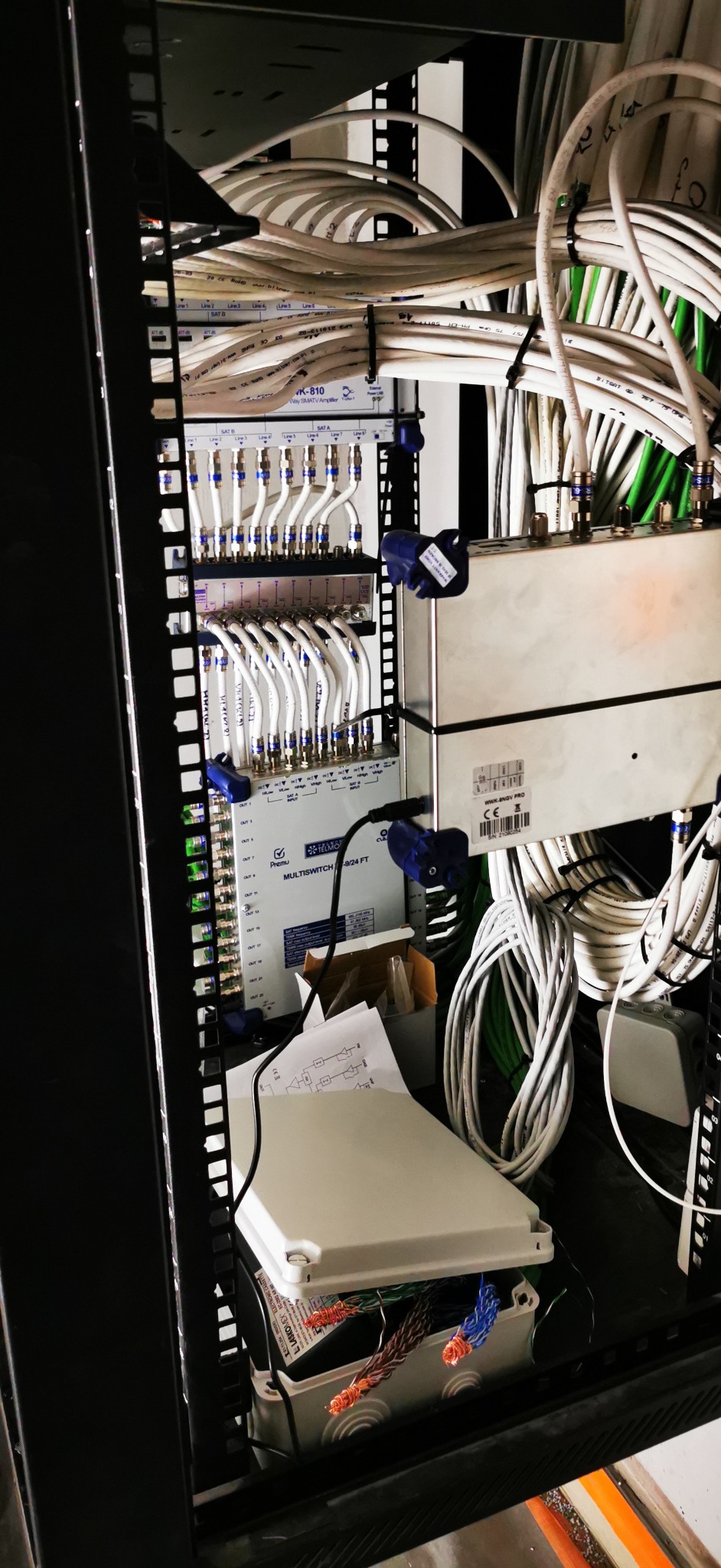 Rozdzielnia kablowa z licznymi przewodami, wzmacniacz sygnału i multiswitch. Instalacja w szafie rack, widoczne kable koncentryczne i złącza.