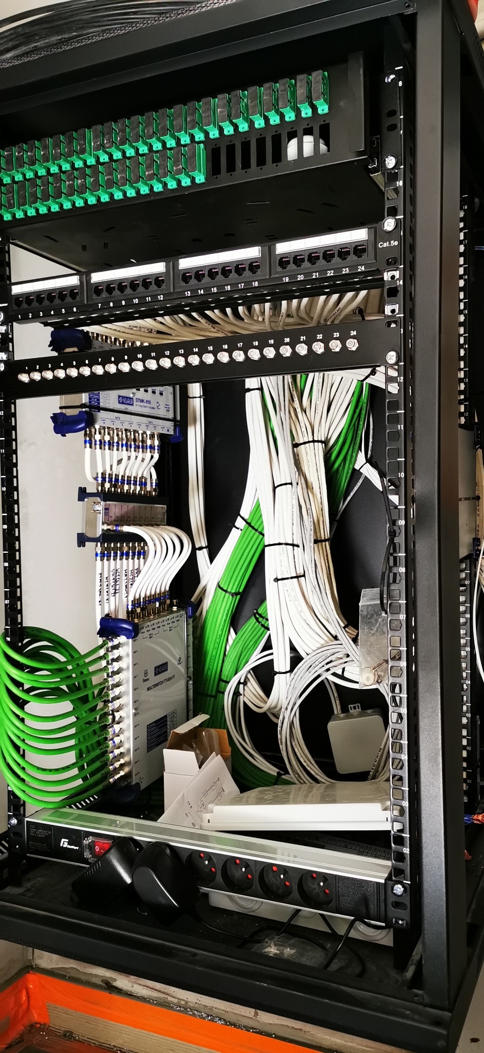 Rozdzielnica elektryczna z zielonymi i białymi kablami w szafie rack. Widoczne złącza, listwa zasilająca i schemat. Instalacja wewnątrz szafy rack.