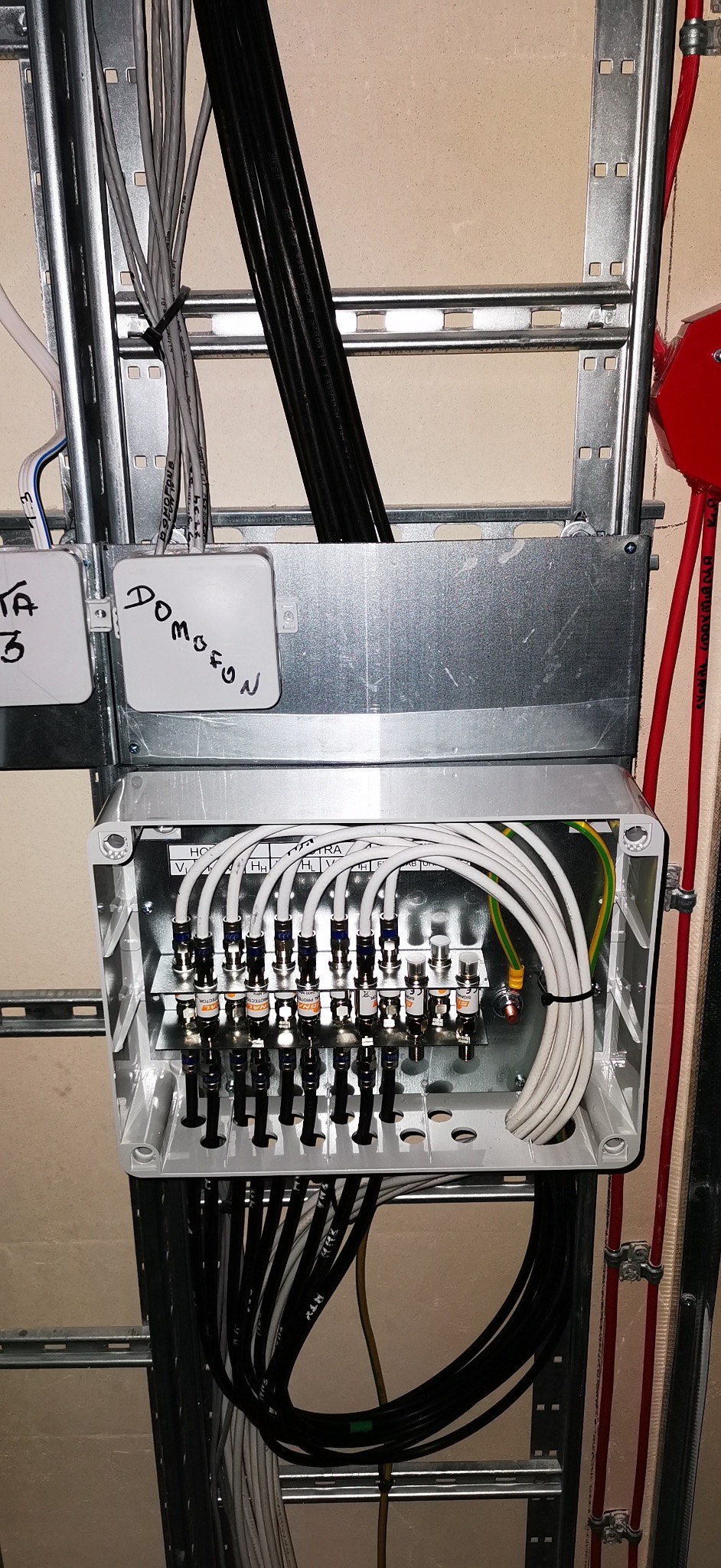 Rozdzielnia antenowa w metalowej obudowie z licznymi przewodami, zamontowana na szynie. Widoczne napisy 'Domofon' na obudowie. Estetyczne ułożenie kabli.