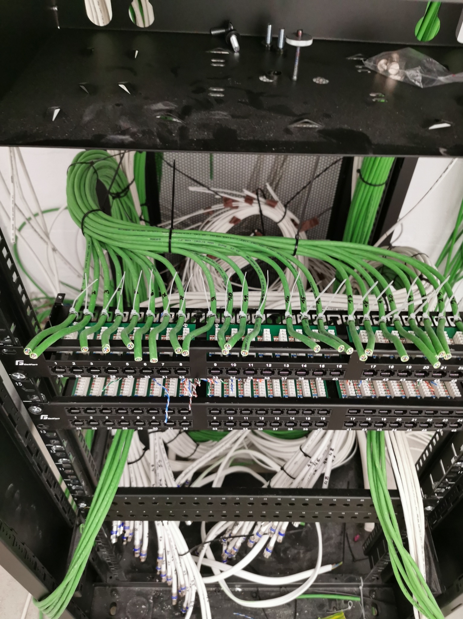 Panel krosowniczy z podłączonymi kablami sieciowymi w kolorach zielonym i białym, zamontowany w szafie rack. Widok z góry, kable uporządkowane.