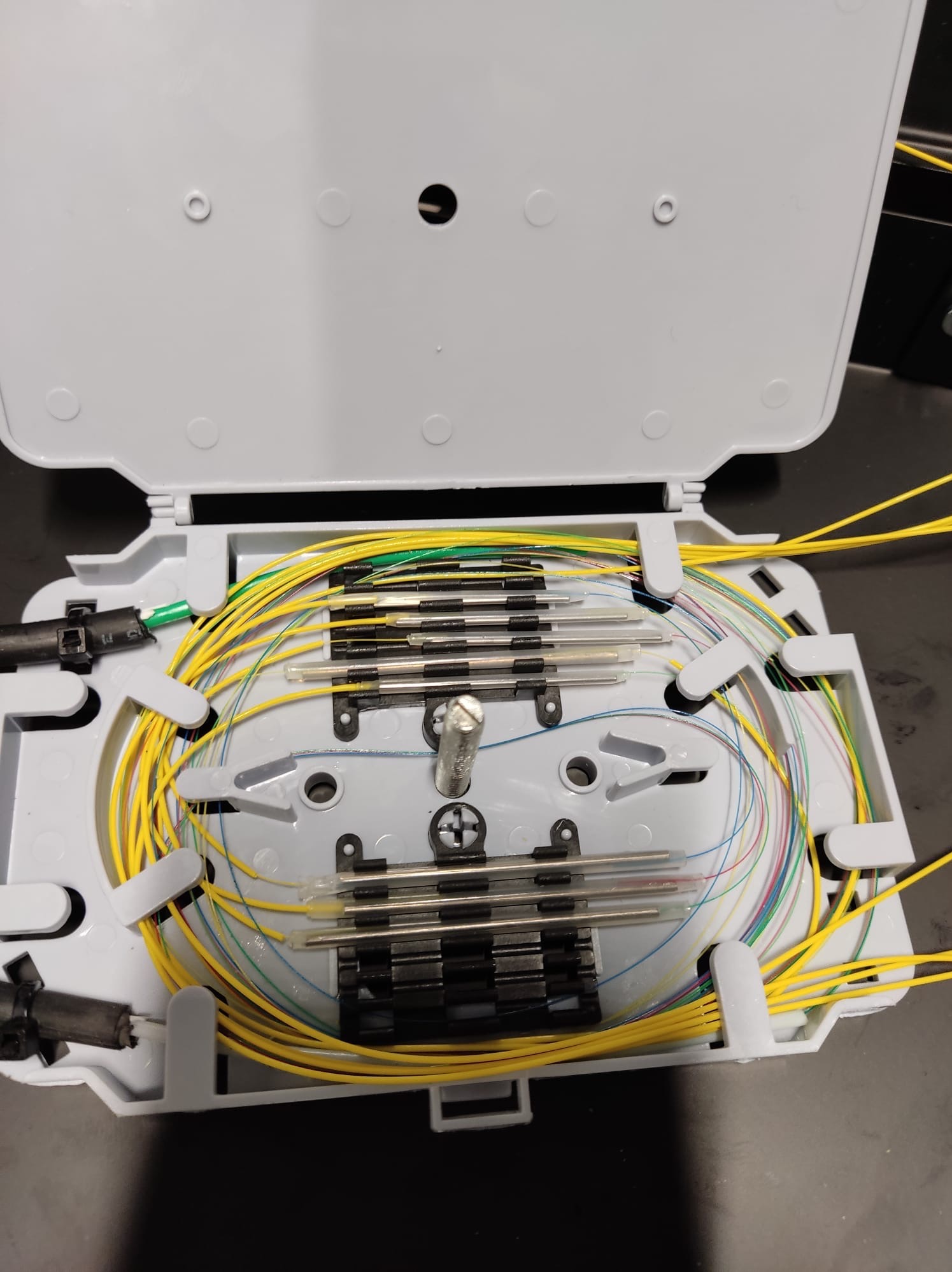 Otwarta skrzynka światłowodowa z precyzyjnie ułożonymi kablami w różnych kolorach. Widoczne złącza i elementy mocujące. Jasne światło podkreśla detale.