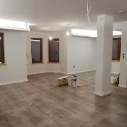 Wnętrze w Cichem k. Czarnego Dunajca w trakcie układania płytek podłogowych, widoczne materiały budowlane i klej, surowe ściany przygotowane do malowania oraz niezabezpieczone kable oświetleniowe.