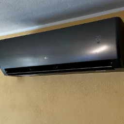 Czarny klimatyzator Gree zamontowany na ścianie o fakturze baranka. Na wyświetlaczu widoczna temperatura 28 stopni. Urządzenie zawieszone blisko sufitu.