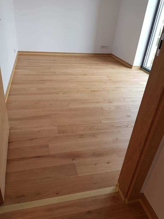 Jasny parkiet dębowy ułożony w nowym pokoju, z widoczną listwą przypodłogową i zabezpieczeniem taśmą malarską przy futrynie drzwi.