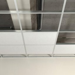 KAR-BUD - Montaż sufitu podwieszanego kasetonowego z widoczną konstrukcją metalową i częściowo zamontowanymi białymi kasetonami. Widoczne instalacje nad sufitem.