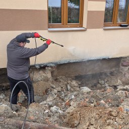 KAR-BUD - Czyszczenie elewacji budynku myjką ciśnieniową przed pracami remontowymi. Widoczne odsłonięte fundamenty i gruz.