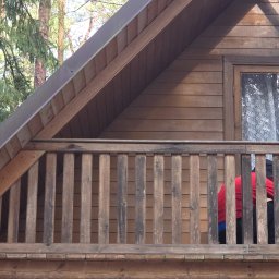 KAR-BUD - Drewniany dom z balkonem i widocznym fragmentem osoby w czerwonej koszulce. Widok z dołu na elewację i balustradę balkonu.