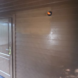 KAR-BUD - Pomazana brązowa ściana z drewnianą boazerią i drzwiami. Widoczny otwór na gniazdko elektryczne. Świeżo pomalowana powierzchnia z połyskiem.