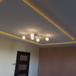 Nowoczesny sufit podwieszany z oświetleniem LED wzdłuż krawędzi, z centralnie umieszczonym żyrandolem z szklanymi kloszami, widok na fragment pokoju z drzwiami i ścianami pomalowanymi na dwa kolory.