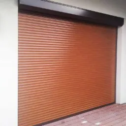 Zamknięta, brązowa osłona okienna na tarasie z drewnianą podłogą, oświetlona przez czarne lampy ścienne.