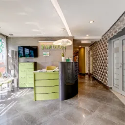 Nowoczesne wnętrze gabinetu lekarskiego z recepcją w odcieniach zieleni i szarości, widoczne logo 'MEDICUS' na ścianie i dekoracyjna ściana z trójwymiarowych elementów w korytarzu.