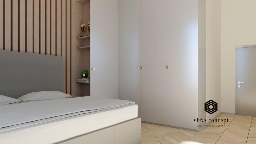 Neutralna sypialnia z łóżkiem z szarym zagłówkiem, drewnianą ścianą z pionowych listew, białymi szafami z okrągłymi uchwytami i otwartą półką z dekoracjami, na parkiecie w jodełkę.