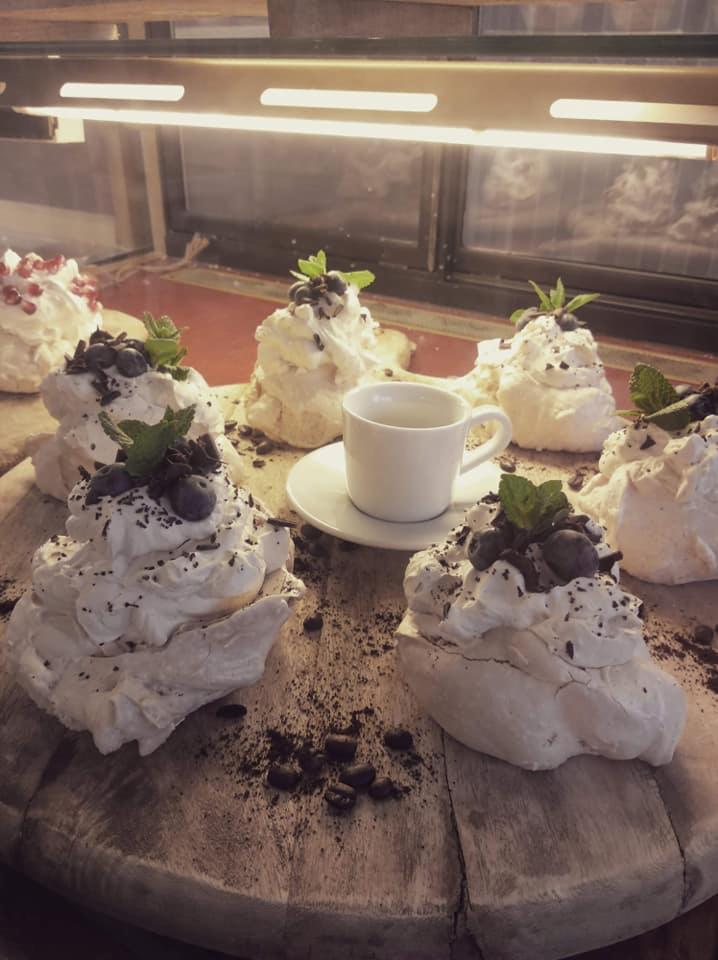 Bezy Pavlova z bitą śmietaną, jagodami i miętą na drewnianej desce, obok biała filiżanka.