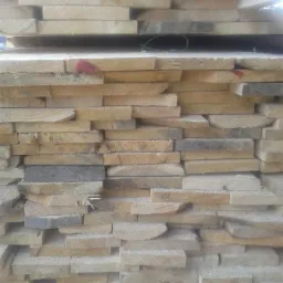 Stos ułożonych desek z jasnego drewna, widoczne ślady po cięciu i niewielkie wióry, na niektórych deskach czerwona etykieta.