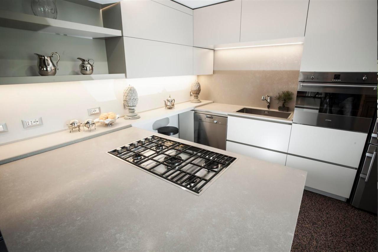 Nowoczesna kuchnia z białymi szafkami, blatem z szarego kamienia i wbudowaną płytą gazową, oświetleniem LED i srebrnymi akcentami.