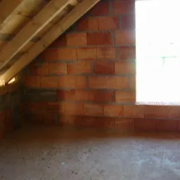 Surowy stan poddasza z cegły ceramicznej z drewnianą konstrukcją dachu i oknem, widoczne niedociągnięcia w spoinowaniu.