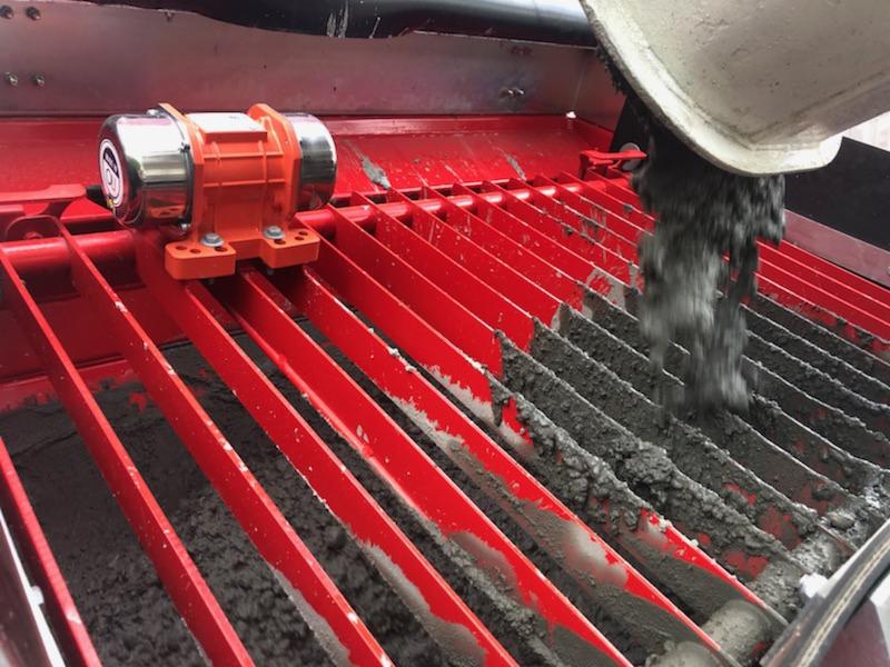 Proces przesiewania świeżego betonu na czerwonym sicie z wibratorem, beton spływa z betonowej rury