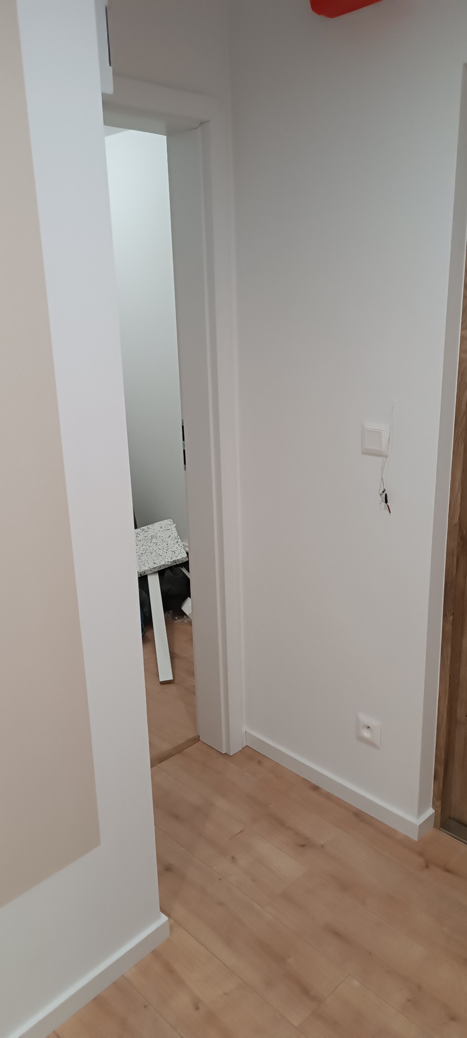 Białe wykończenie wnętrza: pomalowane ściany, drewnopodobne panele, listwy przypodłogowe i ościeżnica. Widoczny fragment gniazdka i włącznika.