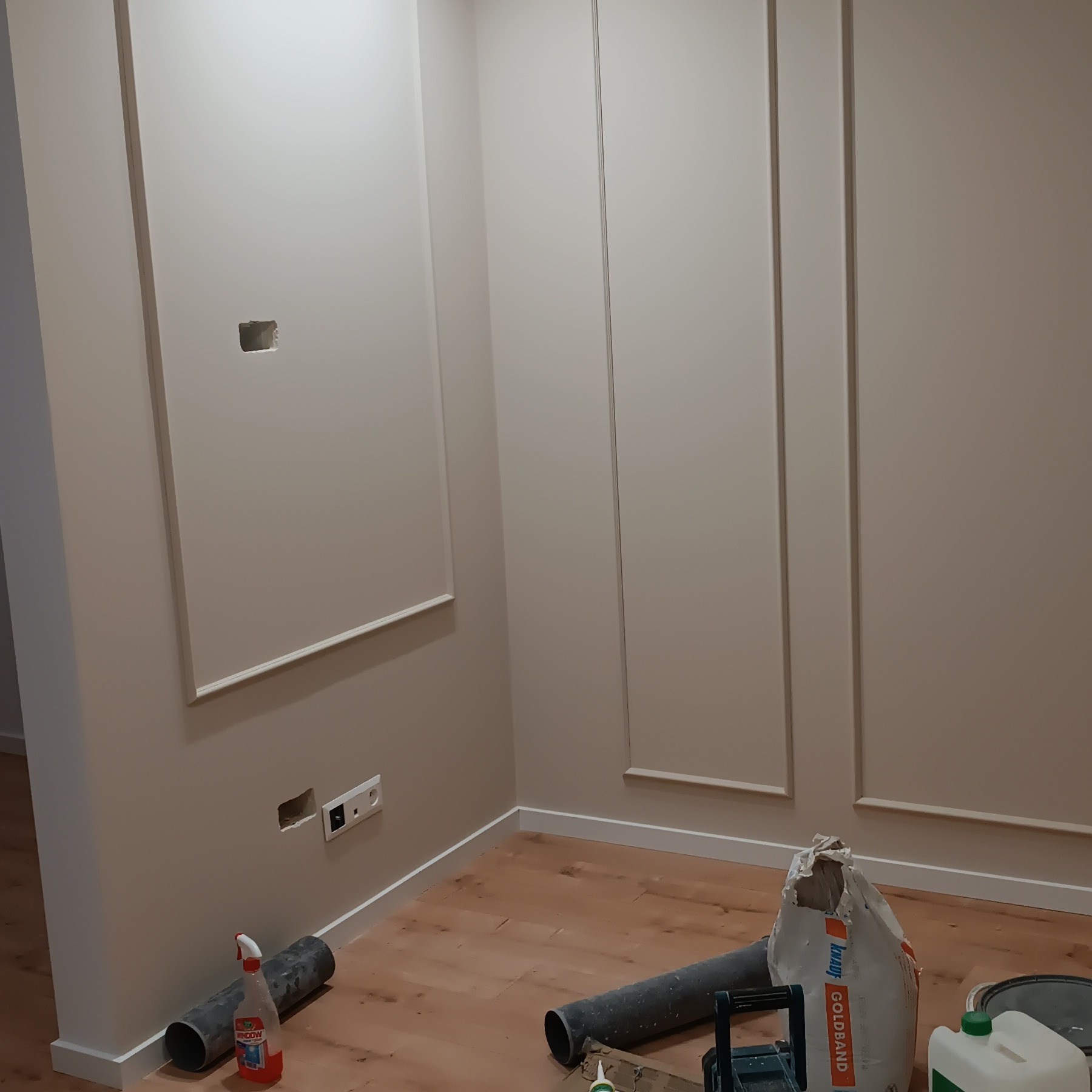 Ściana z dekoracyjnymi listwami i widocznymi puszkami elektrycznymi w trakcie prac wykończeniowych. Na podłodze narzędzia i materiały budowlane.