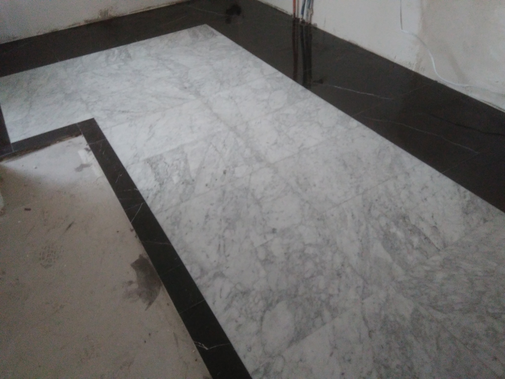 Ułożona marmurowa podłoga z ciemnym obramowaniem, widoczne przewody instalacji elektrycznej przy ścianie.