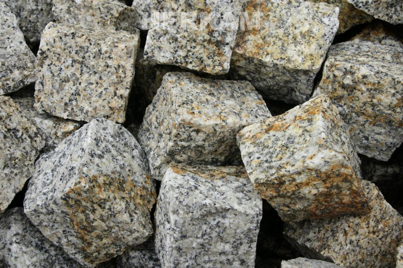 Stos szarych, nieregularnych kostek z widocznymi, drobnymi, ciemnymi i rdzawymi plamkami, ułożonych blisko siebie.