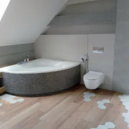 Nowoczesna łazienka na poddaszu z asymetryczną wanną obudowaną mozaiką, wiszącą toaletą i drewnopodobną podłogą z białymi heksagonalnymi wstawkami.