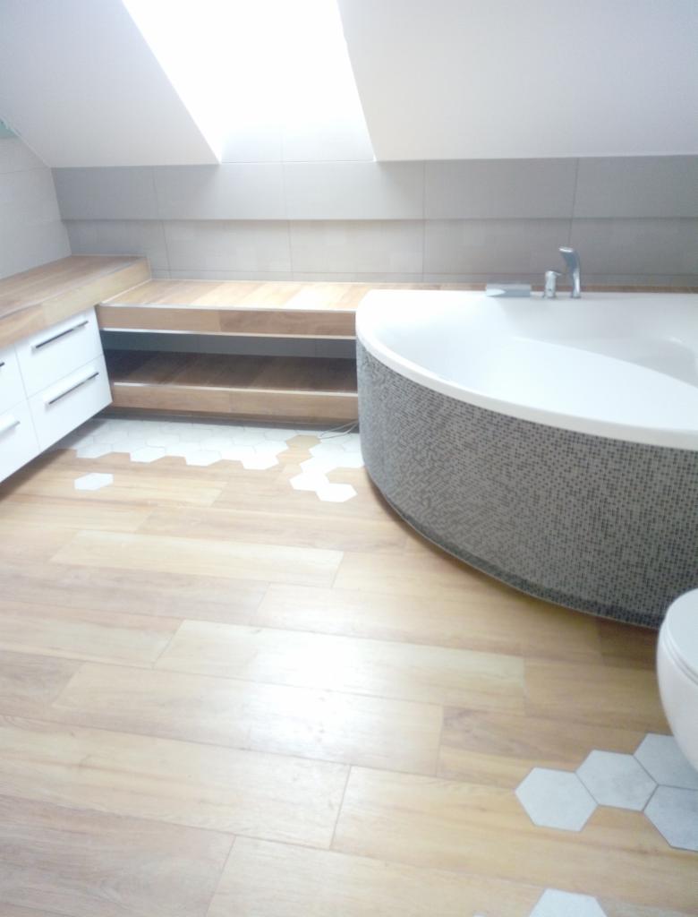 Jasna łazienka na poddaszu z drewnianą podłogą, mozaikową obudową wanny i heksagonalnymi płytkami w strefie podłogi przy wannie.