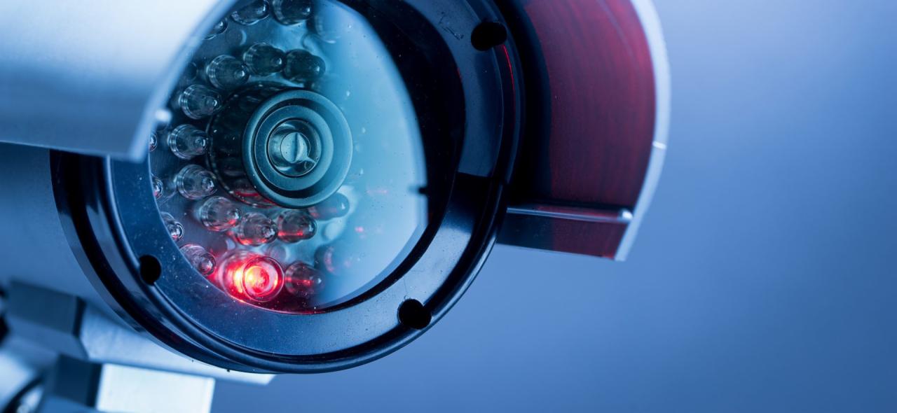 Zbliżenie na kamerę monitoringu z widocznymi diodami IR, część z nich świeci na czerwono, na tle błękitnego tła.