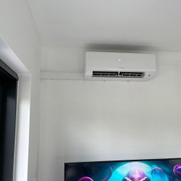 KRW SERWIS - Biały klimatyzator Hyundai zamontowany na ścianie nad telewizorem. Widoczne białe kable w listwie. Minimalistyczny design wnętrza.