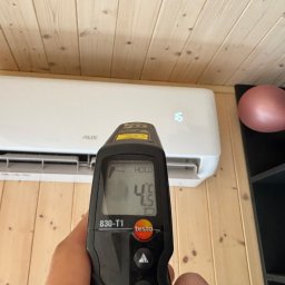 KRW SERWIS - Pomiar temperatury klimatyzatora AUX termometrem Testo 830-T1 na tle drewnianej ściany i czarnego regału z dekoracyjnymi kulami. Wyświetlana temperatura to 4,5°C.