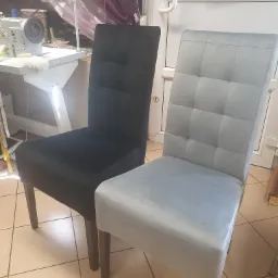 Dwa krzesła z nową tapicerką w odcieniach szarości, jedno czarne, drugie jasnoszare, na tle warsztatu w Krępsku, widoczna maszyna do szycia.