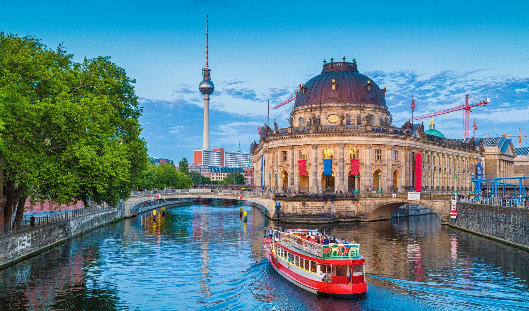 Czerwono-biały statek wycieczkowy płynie po rzece Spree w Berlinie, w tle Muzeum Bode i wieża telewizyjna.