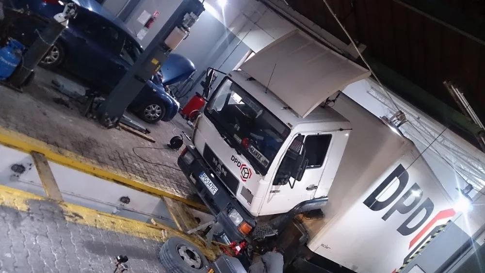 Ciężarówka DPD na podnośniku w warsztacie, widoczne podwozie, opony i inne samochody w tle.