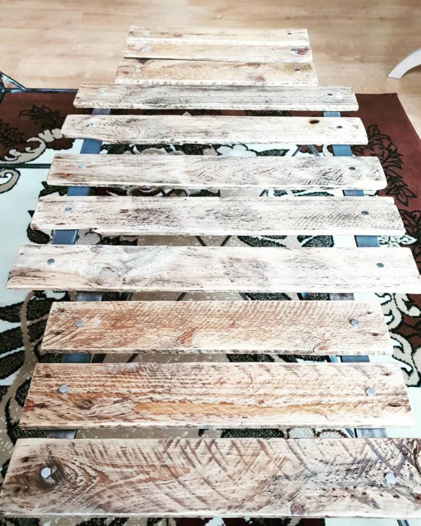 Konstrukcja z desek z odzysku, połączonych metalowymi elementami, widoczna na wzorzystym dywanie.