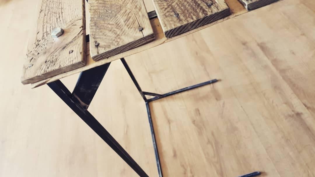 Surowy blat z desek z odzysku, mocowany śrubami do metalowej, spawanej konstrukcji nóg, na tle drewnopodobnej podłogi.