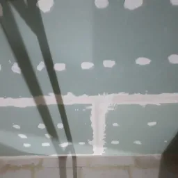 Sufit z zamontowanymi płytami gipsowo-kartonowymi, z widocznymi śladami szpachlowania i ciemnymi cieniami.