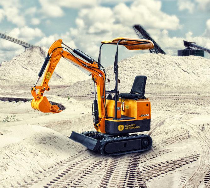 Żółta minikoparka Günter Grossmann CG800 na piaszczystym terenie w Skoczowie, z widocznymi śladami gąsienic i hałdą piasku w tle.