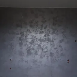 Ściana pokryta dekoracyjną strukturą w odcieniach szarości i srebra, z widocznymi puszkami elektrycznymi i wystającymi przewodami, w trakcie prac wykończeniowych.