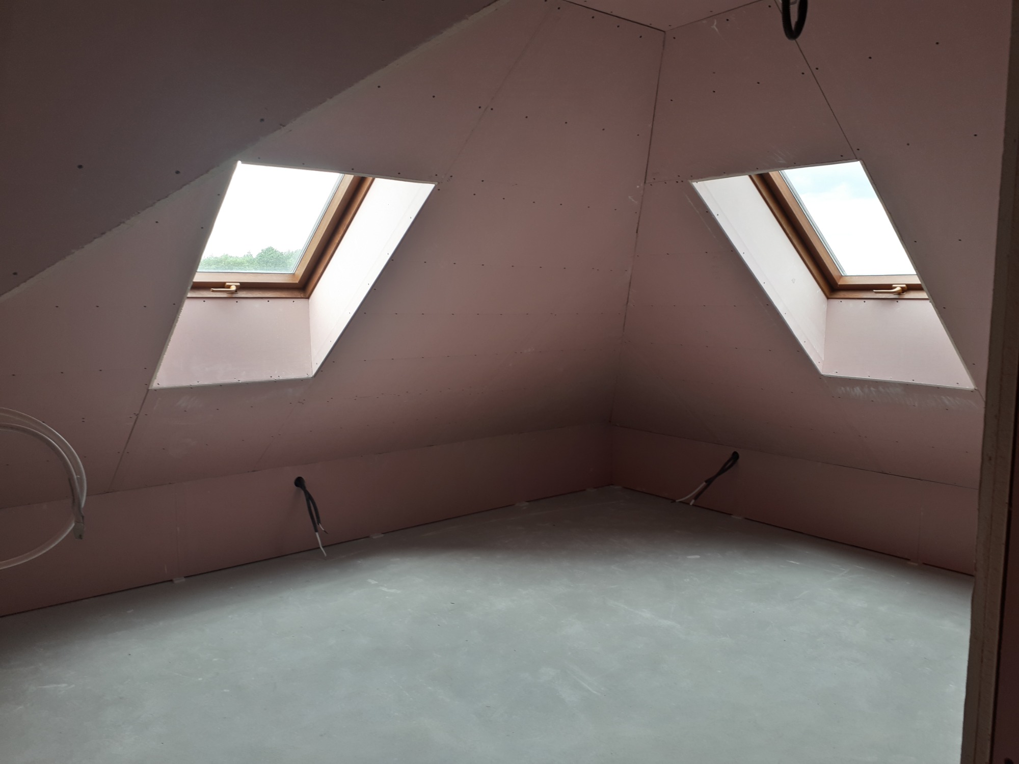 Poddasze z oknami dachowymi, ściany wykończone płytami kartonowo-gipsowymi, widoczne kable elektryczne i szpachlowane łączenia płyt.