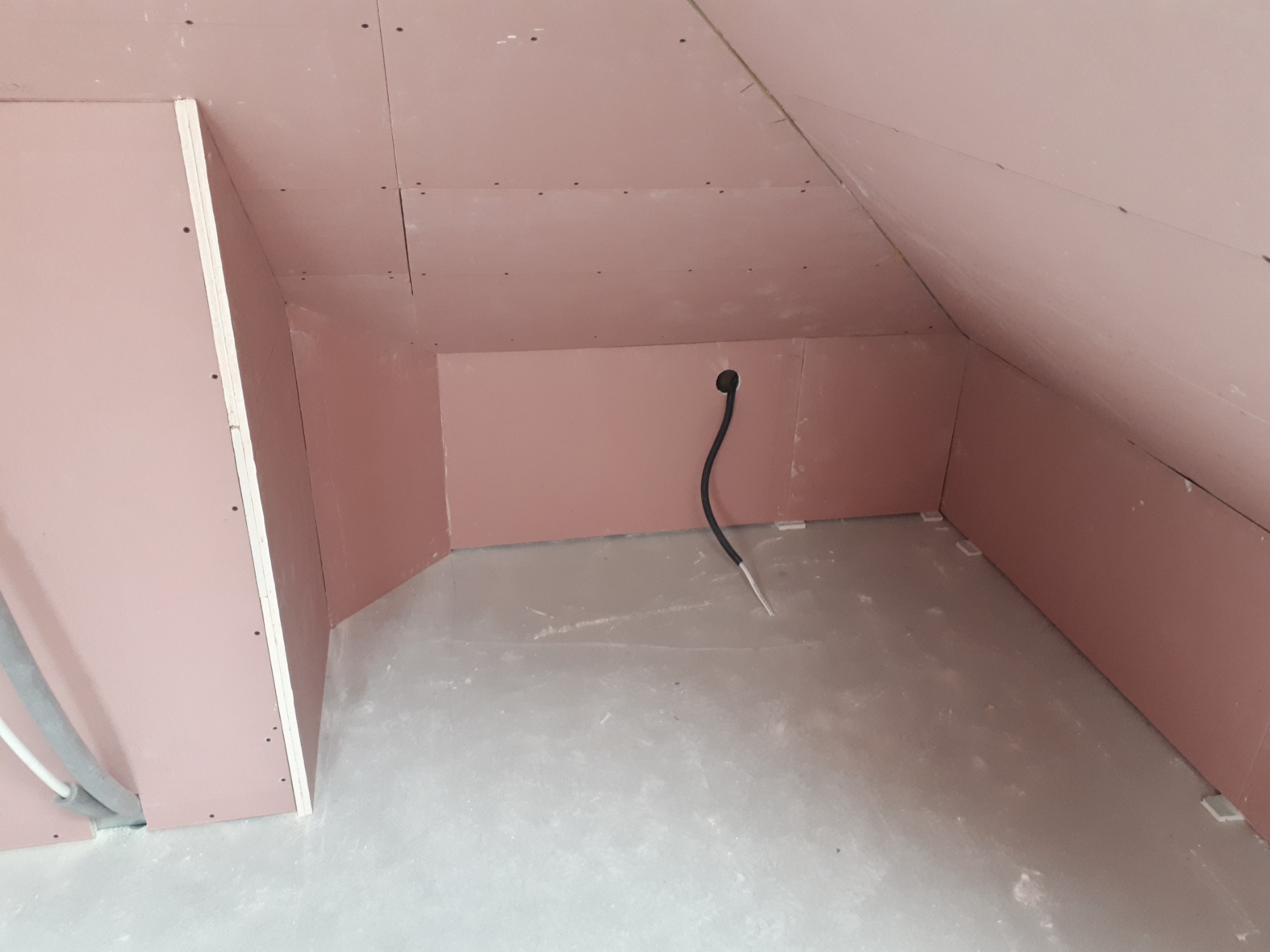 Montaż płyt karton-gips na poddaszu, widoczne łączenia płyt i wystający kabel elektryczny ze ściany.