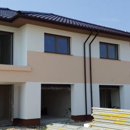 Adrian marek - Dwukondygnacyjny dom w trakcie prac elewacyjnych, z widocznym ociepleniem w formie płyt styropianowych ułożonych przed budynkiem, oraz częściowo pomalowaną elewacją w kolorach białym i beżowym.