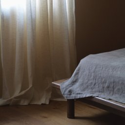 Madde studio Sp. z o.o. - Minimalistyczna sypialnia: drewniana podłoga, lniana pościel na niskim łóżku, delikatne zasłony wpadające do pokoju. Stonowana kolorystyka, naturalne materiały.