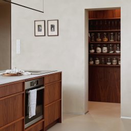 Madde studio Sp. z o.o. - Minimalistyczna kuchnia z drewnianymi szafkami, marmurowym blatem i spiżarnią w tle. Dwa zdjęcia w ramkach na ścianie. Oświetlenie liniowe.